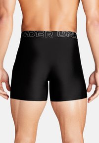 Schwarze Boxershorts aus glattem Material. Mit einem breiten elastischen Bund, auf dem "UNDER" in Schwarz und Silber gedruckt ist.