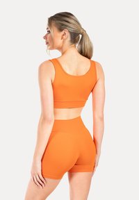 Sujetador deportivo naranja y pantalones cortos de talle alto hechos de tejido elástico. Textura suave, diseño ajustado y sin logotipos ni patrones visibles.