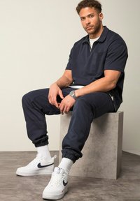 Marineblauwe rits-t-shirt met korte mouwen en bijpassende joggers, met een voorzak. Gecombineerd met witte Nike sneakers en witte crew sokken.