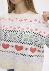 Cream-colored sweater with a festive pattern featuring red hearts, green holly leaves, and snowflakes. Soft texture and ribbed neckline.