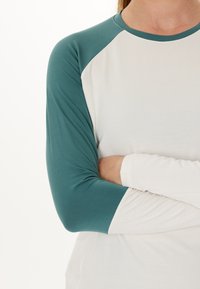 Raglanshirt med hvid krop og teal-grønne ærmer. Lavet af blødt stof med en glat tekstur, der fremhæver det afslappede design.