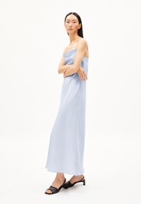 Robe maxi sans bretelles bleu clair avec un design fluide. Le tissu est lisse, associé à des sandales à talons noires avec une bride texturée.
