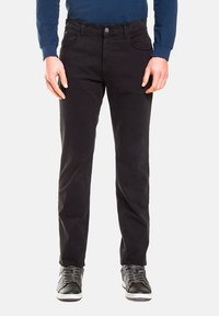 Pantaloni neri in misto cotone con una vestibilità slim, dotati di tasche anteriori, chiusura con bottone e dettagli di cucitura sottili. Abbinati a sneakers nere.