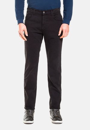 Pantaloni neri in misto cotone con una vestibilità slim, dotati di tasche anteriori, chiusura con bottone e dettagli di cucitura sottili. Abbinati a sneakers nere.