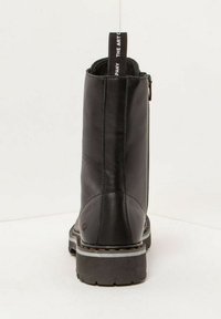 Bottine en cuir noir avec une texture lisse, bout rond, fermeture éclair sur le côté et semelle contrastante avec un motif cranté.