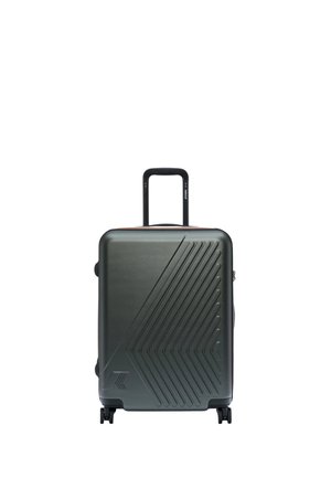 Valigia rigida grigio scuro con motivo a chevron, manico telescopico esteso e quattro ruote girevoli su sfondo bianco.