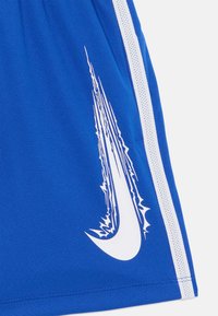 Blå atletiska shorts gjorda av lättviktsmaterial. Har vita sidostråk och en stor vit Nike-logotyp med en dynamisk design.