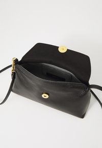 Sac en cuir noir avec une finition lisse, doté d'une fermeture à pression dorée et d'une bandoulière amovible, mettant en avant un design minimaliste.