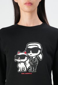 Felpa nera con un grafico che rappresenta un personaggio dei cartoni animati e un gatto, entrambi con occhiali da sole. Il design include dettagli rossi.