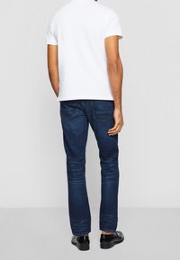 T-shirt en coton blanc, jeans en denim bleu, teinte sombre, coupe slim, design droit, couture minimaliste, avec des chaussures habillées noires.