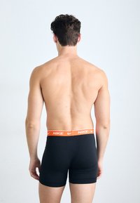 Black moisture-wicking boxer briefs with an orange Nike logo on the elastic waistband. Smooth texture, close-fitting design.