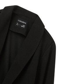 Blazer nero realizzato in tessuto liscio, con revers a punta e un'etichetta con le informazioni sulle taglie per età 12/13 e altezza 152/158.