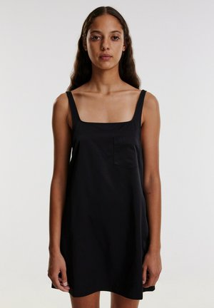 Black sleeveless dress with a square neckline and a small chest pocket. Made from a smooth fabric, it has a relaxed fit and simple design.