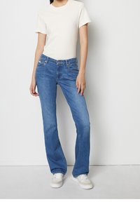 Ljusblå denimbyggevast med hög midja, fem fickor och kontrasterande sömmar. Matchas med en figurnära ribbad vit t-shirt och sneakers.