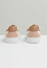 Baltie apavi ar gludu ādas virsu, rozā zamša akcentiem uz papēža un baltu teksturētu gumijas zoli. Zelta zīmols aizmugurē.