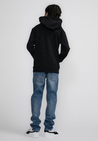 Felpa nera con un design inciso discreto, abbinata a jeans di denim azzurro chiaro. Sneakers bianche con accenti neri e suola flessibile.