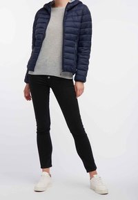Marineblauer Pufferjacke mit Kapuze, grauem langärmligem Oberteil, schwarzen Slim-Fit-Jeans und weißen Sneakers; verfügt über eine gesteppten Textur und einen Frontreißverschluss.