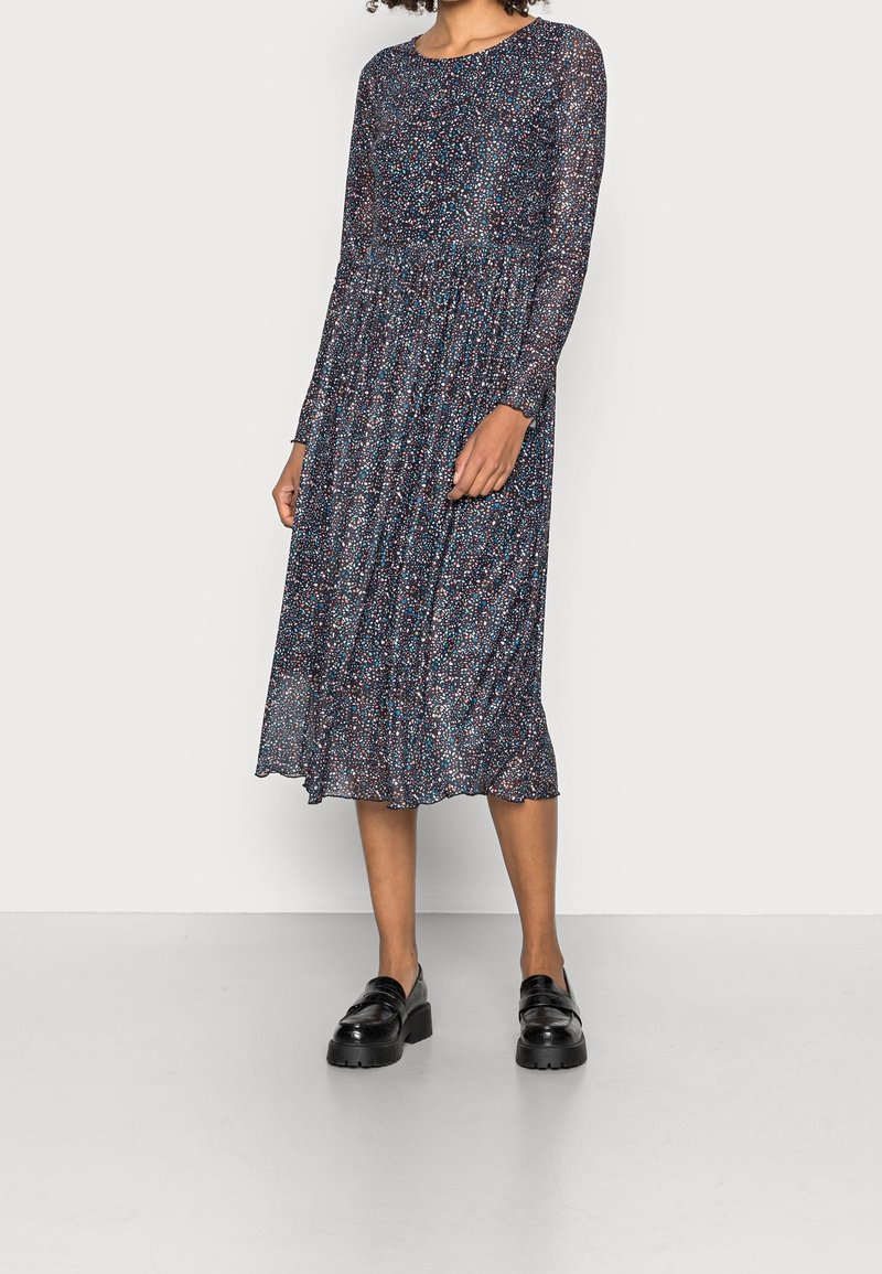 Femme portant une robe midi manches longues bleu marine avec un petit imprimé floral multicolore, associée à des mocassins chunky noirs.