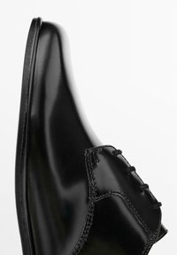 Chaussure en cuir noir avec une finition brillante, bout arrondi et couture décorative le long de la zone de laçage. Design élégant et épuré.