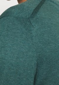 Maglione lavorato a maglia teal con collo a giro, caratterizzato da un tessuto testurizzato e dettagli nelle cuciture delle spalle, progettato per comfort e abbigliamento casual.