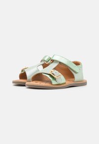 Sandalias metálicas verde claro con un diseño abierto, que cuentan con dos correas ajustables y un detalle de hebilla en el costado. Suela plana de color beige.