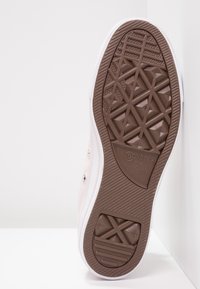 Beige Converse sneakersula med ett strukturerat brunt gummimönster och vit gummikant. Har logotyp och en tydlig greppdesign.