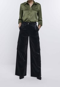 Olivgrön satinsskjorta med polerade knappar, matchad med svarta, vida cargobyxor med glänsande yta, fickor med lappar och bältesöglor.