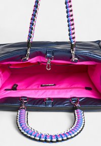 Glanzende marineblauwe handtas met gevlochten hengsel in blauw, roze en grijs. Het interieur heeft een felroze voering en meerdere zakken met ritsen.