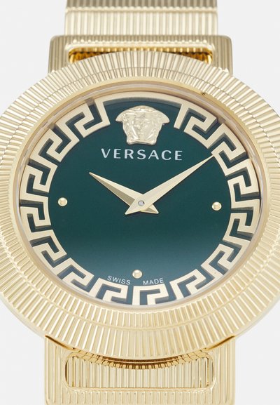 Kullatud rihmaga käekell ribatud bezeliga, rohelise näo, Medusa emblemiga, Kreeka võtme mustriga ja kuldsete kätega. Šveitsi valmistatud metallist rihmaga.