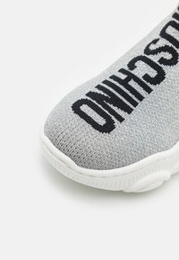 Graue gestrickte Sportschuhe mit schwarzem Text, weißer Sohle und strukturiertem Obermaterial. Verfügt über ein Schlupfdesign für einfaches Anziehen.
