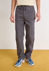 Grå, lette, drawstring bukser med en avslappet passform. Stoffer virker glatte med en lett glans. Brukt med blå sportsko.
