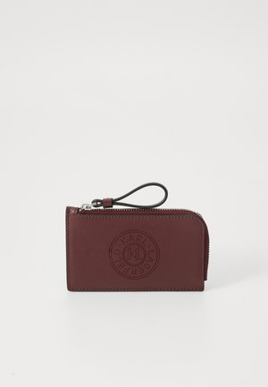 Burgundy leather wallet with a zip closure, featuring a debossed circular logo on the front and a convenient wrist strap. Compact rectangular shape.