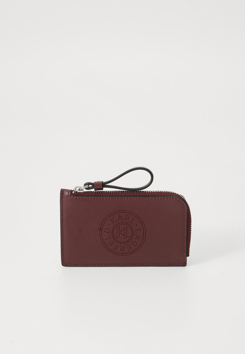 Portafoglio in pelle borgogna con chiusura a zip, caratterizzato da un logo circolare impressa sul davanti e da un comodo cinturino per il polso. Forma rettangolare compatta.
