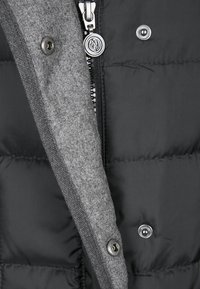 Geïsoleerde zwarte pufferjack met een grijze gebreide kraag; voorzien van een rits, drukknoopsluiting en een gelabelde ritstrekker. Gestructureerde stof.