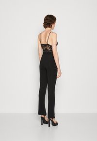 Combinaison noire avec un dos en dentelle ajusté, des bretelles spaghetti et des jambes évasées. Fini avec des sandales noires à talons hauts pour ajouter de la hauteur.