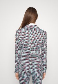 Ensemble de costume à motifs présentant un design géométrique multicolore en rouge, noir et bleu clair. Coupe ajustée avec une fermeture à un bouton.