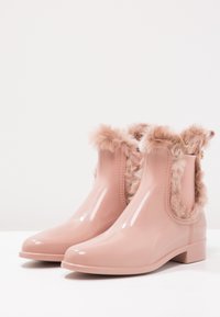 Botines rosa brillantes con ribete de piel sintética alrededor de la abertura y tacones bajos en una superficie blanca.