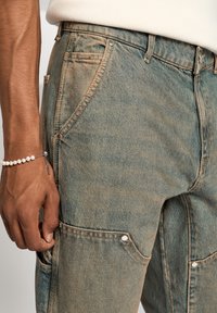 Ljusblå denim cargo-byxor med flera fickor, synlig syddning och silverfärgad hårdvara. Strukturerad tyg med en blekt finish.