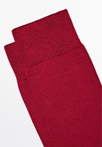 Bordeaux beenwarmers gemaakt van zachte, textuurstof, met een geribbelde bovenkant en een gladde body, omgevouwen aan de bovenkant om een gelaagd ontwerp te tonen.