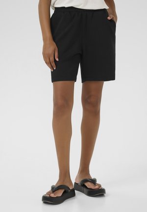 Shorts neri in misto cotone con vita elasticizzata e tasche laterali. Indossati con sandali neri con tacco alto. Texture liscia, lunghezza al ginocchio.