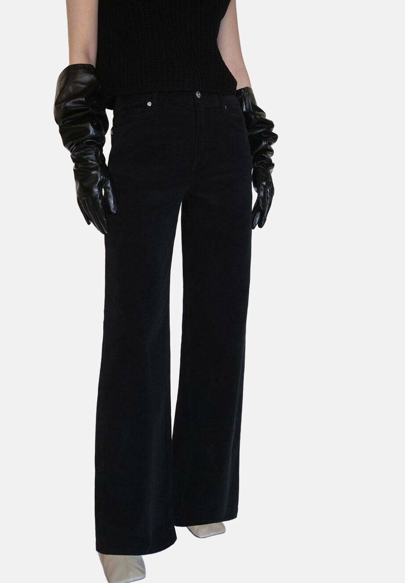 Pantalons larges noirs en tissu texturé, avec une taille haute et des boutons avant en métal argenté. Accompagnés de longs gants noirs.