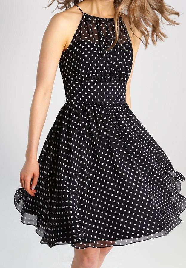 Schwarzes Kleid mit Pünktchenmuster, enganliegendem Oberteil und fließendem Rock, mit einem transparenten Überzug am Ausschnitt und Halterneck-Trägern.