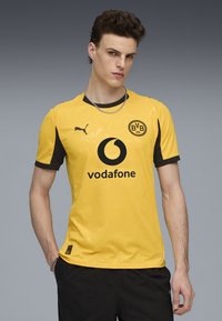 Geltona futbolo marškinėliai su juodais akcentais, su Puma ženklu, Vodafone prekių ženklu ir apvaliu klubo emblema. Tekstūruota medžiaga ir trumpomis rankovėmis.