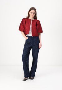 Red textured cropped jacket over a white top, paired with navy pants featuring white polka dots. Black heels complete the outfit.