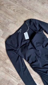 Schwarzes langärmliges Kleid mit gerafftem Seitendetail, flach auf einem Holzboden liegend, mit Abercrombie & Fitch Etikett und Label im Krageninneren.