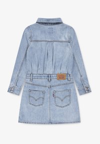 Vestuário de ganga de manga longa azul clara com colarinho, bolsos traseiros, passadores para cinto, punhos com botão e um emblema de marca em couro na cintura.