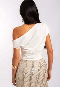 Top blanc à épaule unique avec des manches courtes et une taille froncée. Associé à une jupe beige ornée de sequins argentés en motif zigzag.