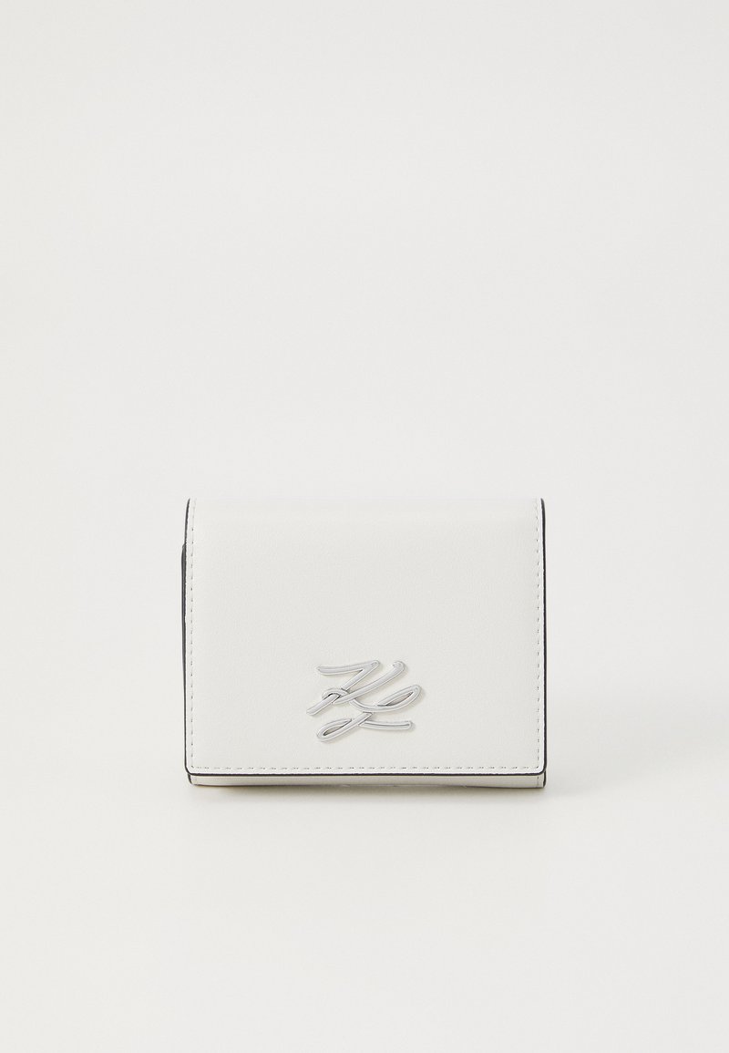 Balts mākslīgās ādas maks ar sudraba logotipu priekšpusē, ar taisnstūra formu un kontrastējošām melnā diega detaļām.