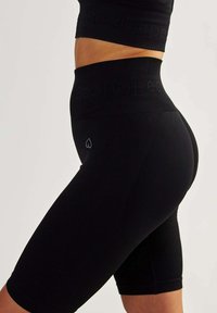 Black ribbed cycling shorts feature high waistband and small heart logo. Made from stretchy material, designed for comfort and movement.