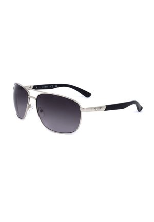 Occhiali da sole Guess con montatura metallica, lenti scure e terminali delle aste in plastica nera, mostrati inclinati su sfondo bianco.
